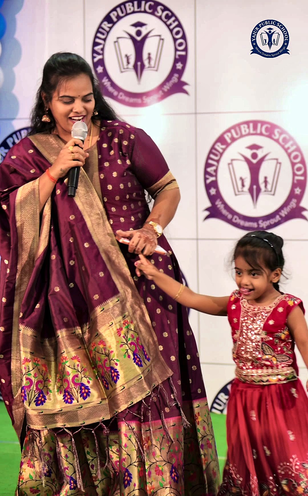 A Yajur teacher on stage with a smiling young student at the Happiness Carnival