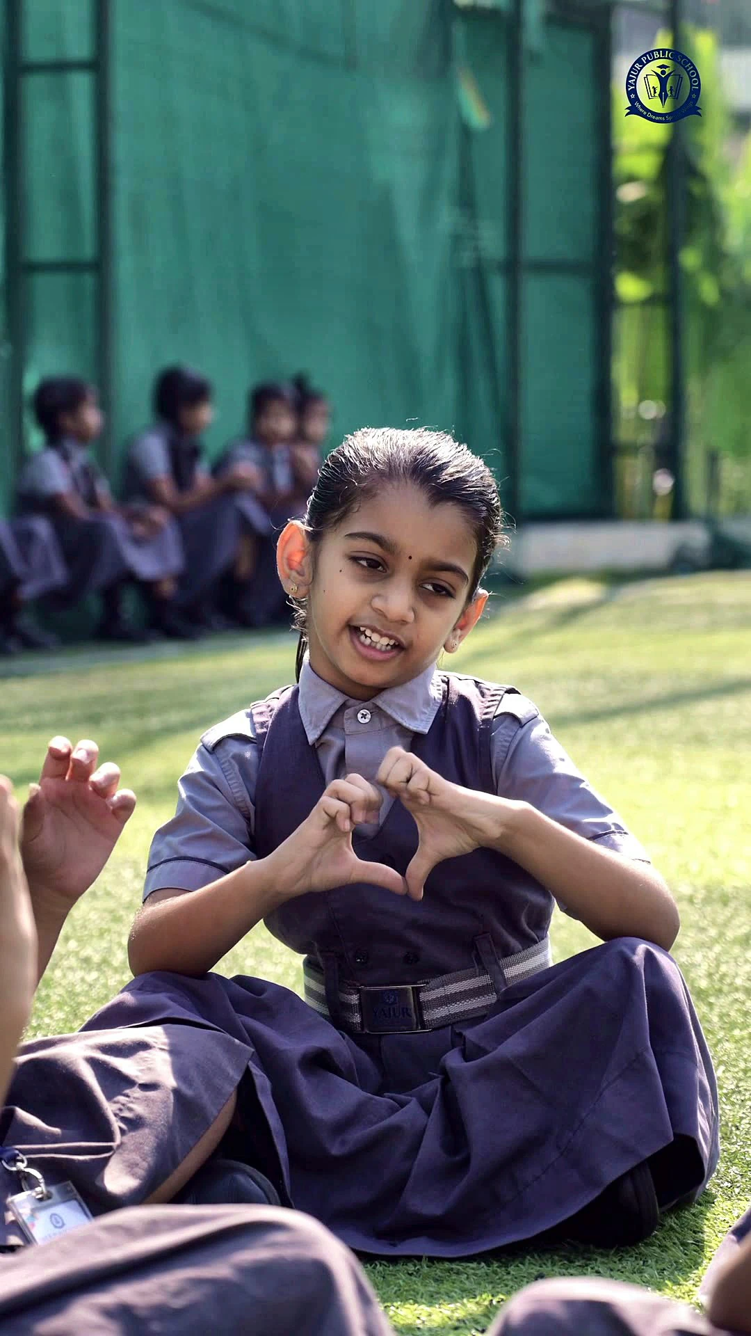 A student making a heart with her hands on the lawn