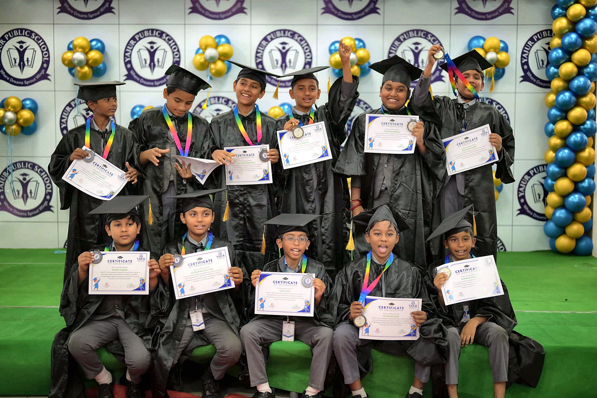 Yajur students in graduation gowns holding their certificates and medals